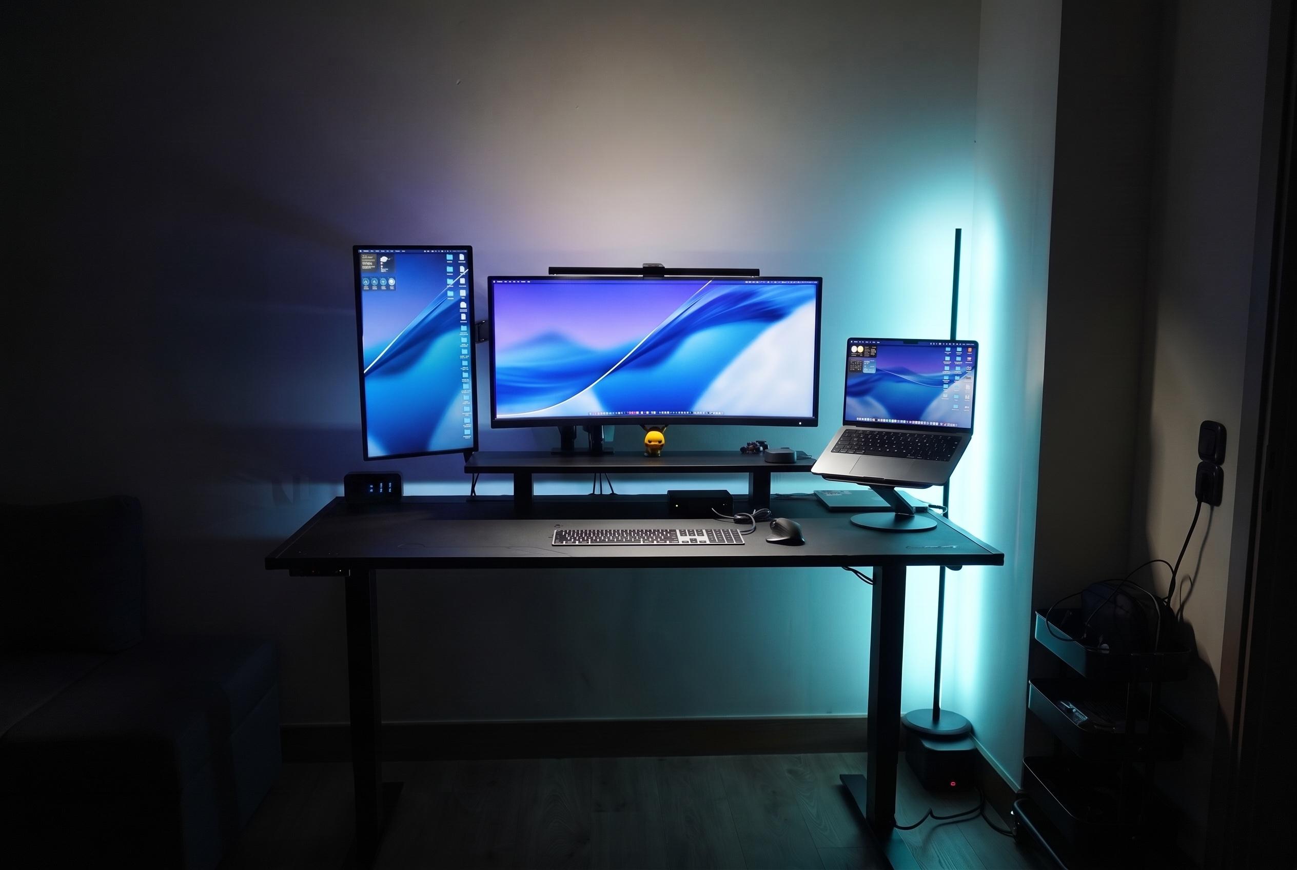The desk at night, screens on a blue wallpaper and the Nanoleaf light bar on cyan